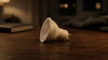 A single LED bulb lying on a wooden table, softly lit by warm light. A closed book and a blurred fabric in the background create a cozy atmosphere.