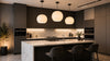 Modern kitchen with dark cabinets, marble island, and three large pendant lights. Three gray chairs at the island add a sleek, cozy touch.
